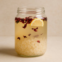 A clear glass jar filled with water kefir grains fermenting in liquid, with colorful fruit pieces floating inside, set against a bright and natural background.