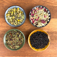 Four bowls with different types of dried herbs and spices on a wooden surface