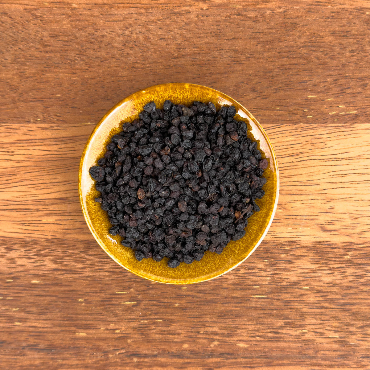 Gold bowl filled with dark berries on a wooden surface
