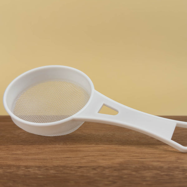 White plastic strainer on a wooden surface with a yellow background