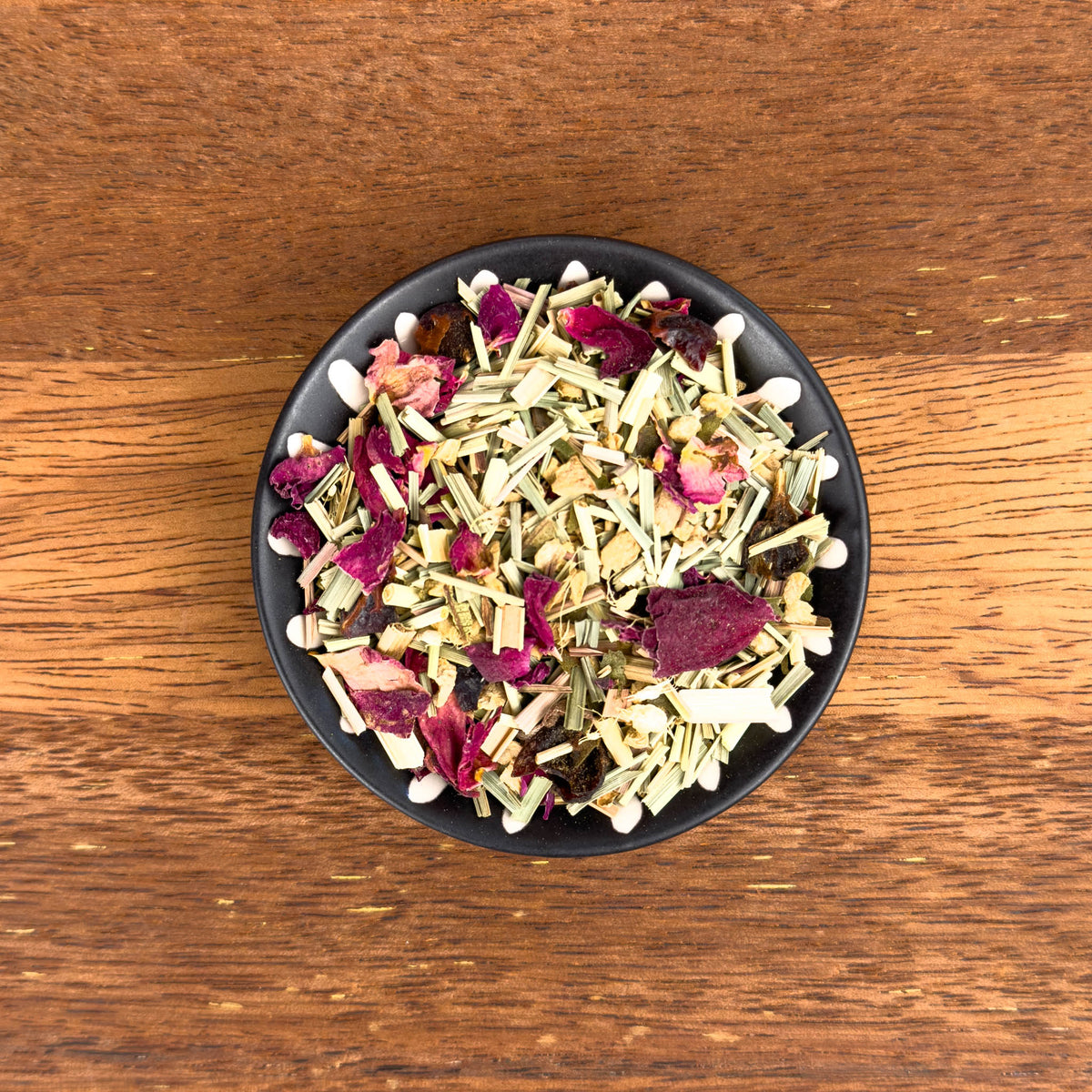 Black bowl filled with a mix of dried herbs and flowers on a wooden surface