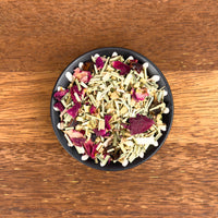 Black bowl filled with a mix of dried herbs and flowers on a wooden surface