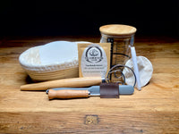 Front view of The Fermentation Station’s Sourdough Master Baking Kit, featuring dehydrated starter, banneton, dough whisk, silicone spatula, lame, and other baking tools.