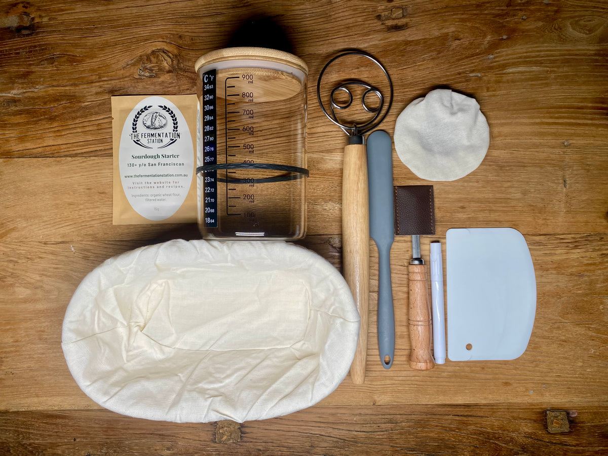 Top-down view of The Fermentation Station’s Sourdough Master Baking Kit, featuring dehydrated starter, banneton, dough whisk, silicone spatula, lame, and other baking tools.