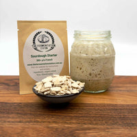 Sourdough starter, package, bubbling starter in a jar, and bowl on a wooden surface with 'The Fermentation Station' branding.