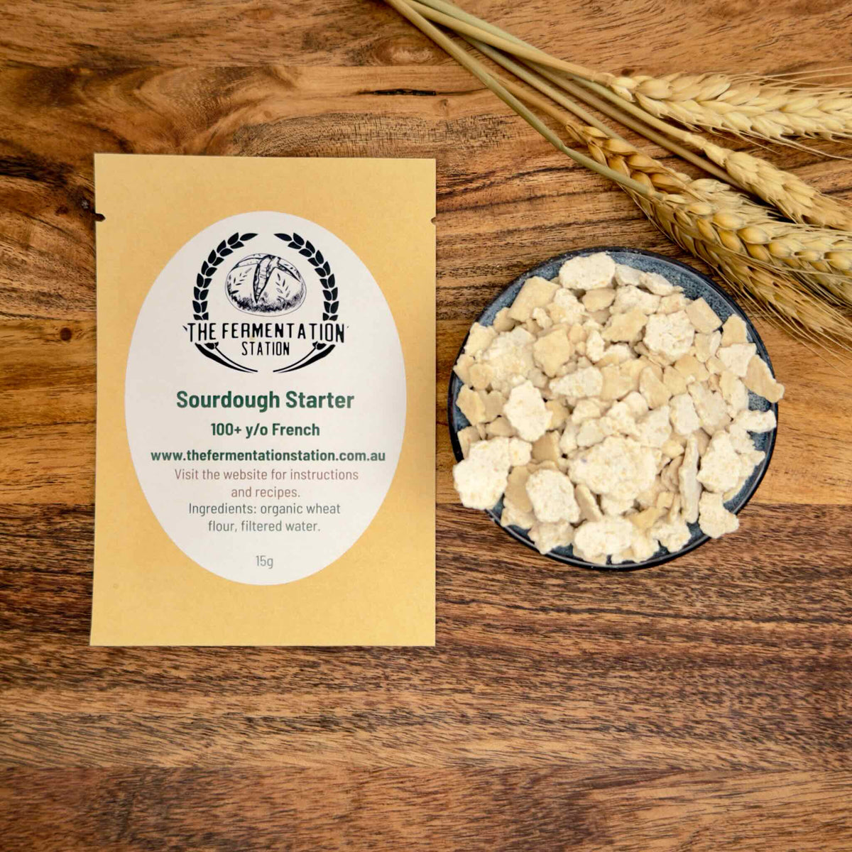 Sourdough starter package with a bowl of dehydrated starter and wheat ears on a wooden surface