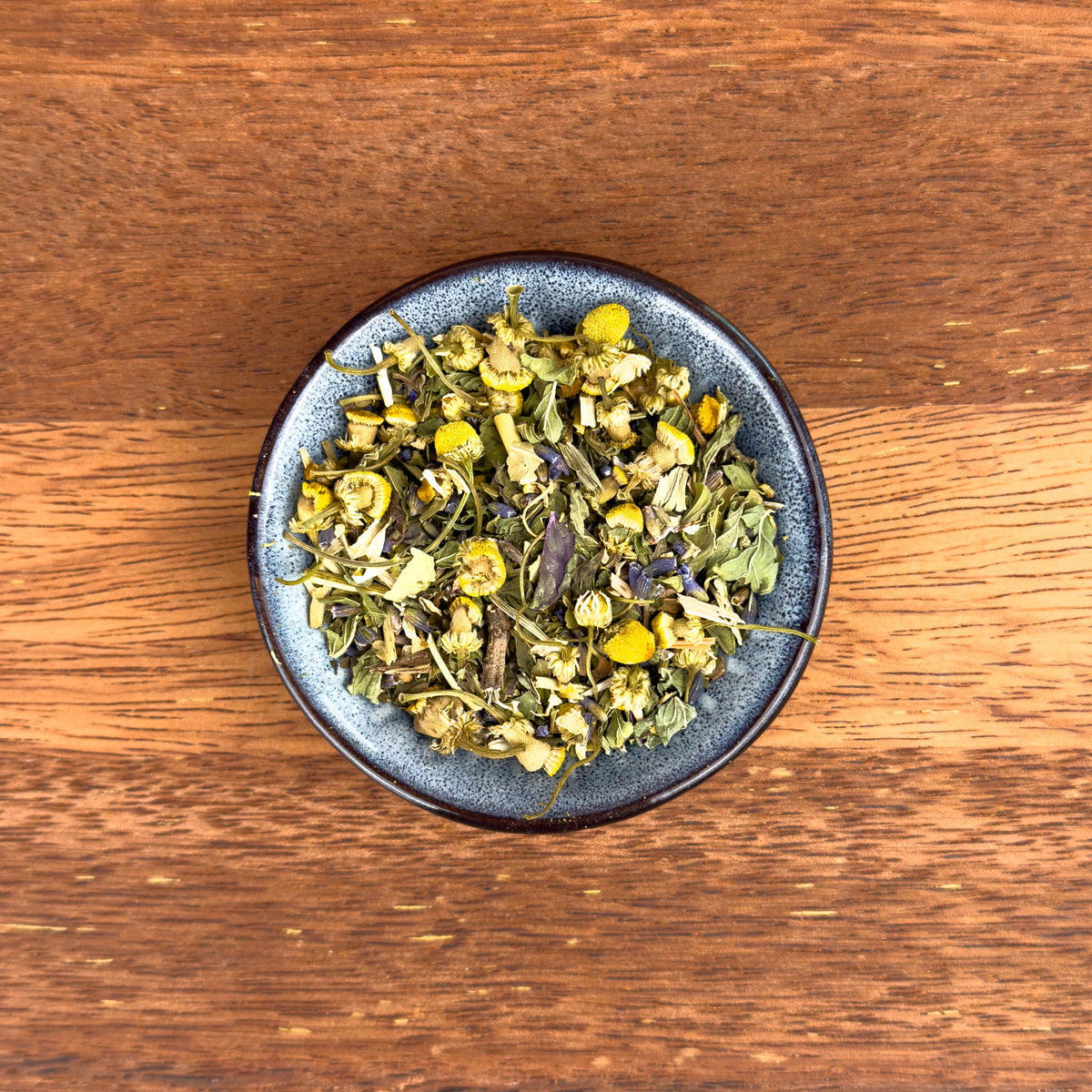 Dried herbs and flowers in a dark blue bowl on a wooden surface